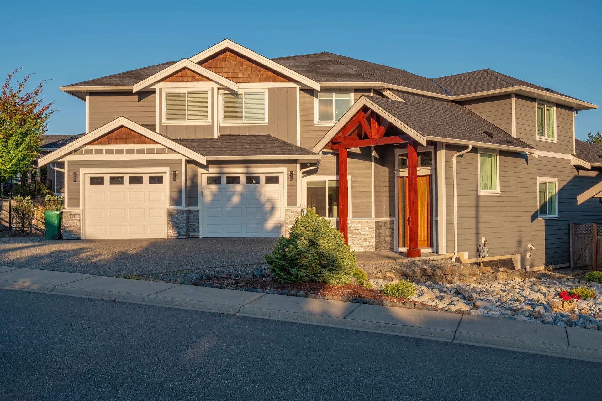 A large gray house with a white garage door is sitting on the side of the road.
